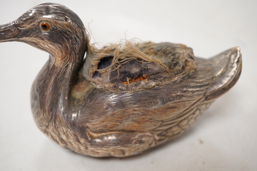 An Edwardian novelty silver mounted pin cushion, modelled as a duck, by Abrahall & Bint, engraved with 'feather' decoration and glass eyes, Birmingham, 1906, length 94mm, height 59mm(a.f.).